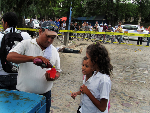 Dos niñas compran minutas frente al cadáver de Roberto Funes de 42 años en La Ceiba, Honduras.